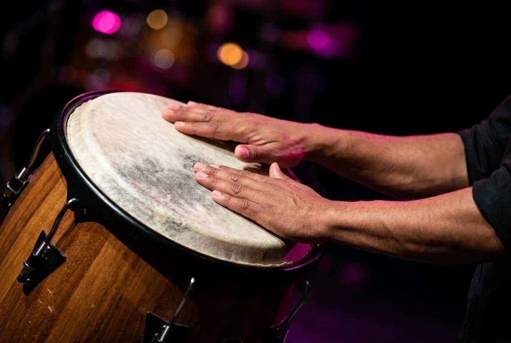 A percussionist's hands striking the head of a wooden conga drum